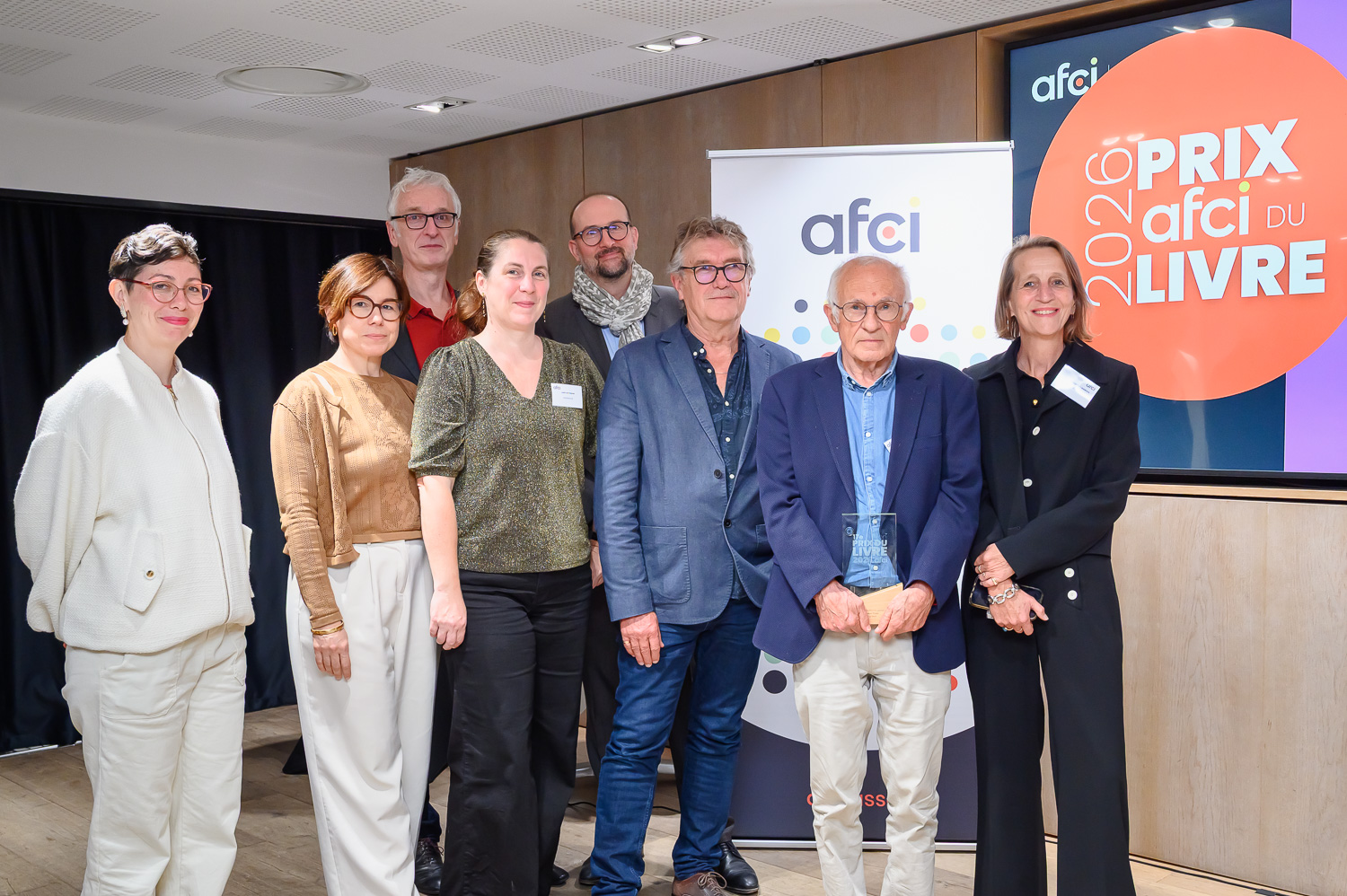 Photo de groupe de François Dubet tenant son trophée, entouré de sept membres du jury, devant le logo de l’Afci et l’écran « Prix Afci du Livre 2026 ».